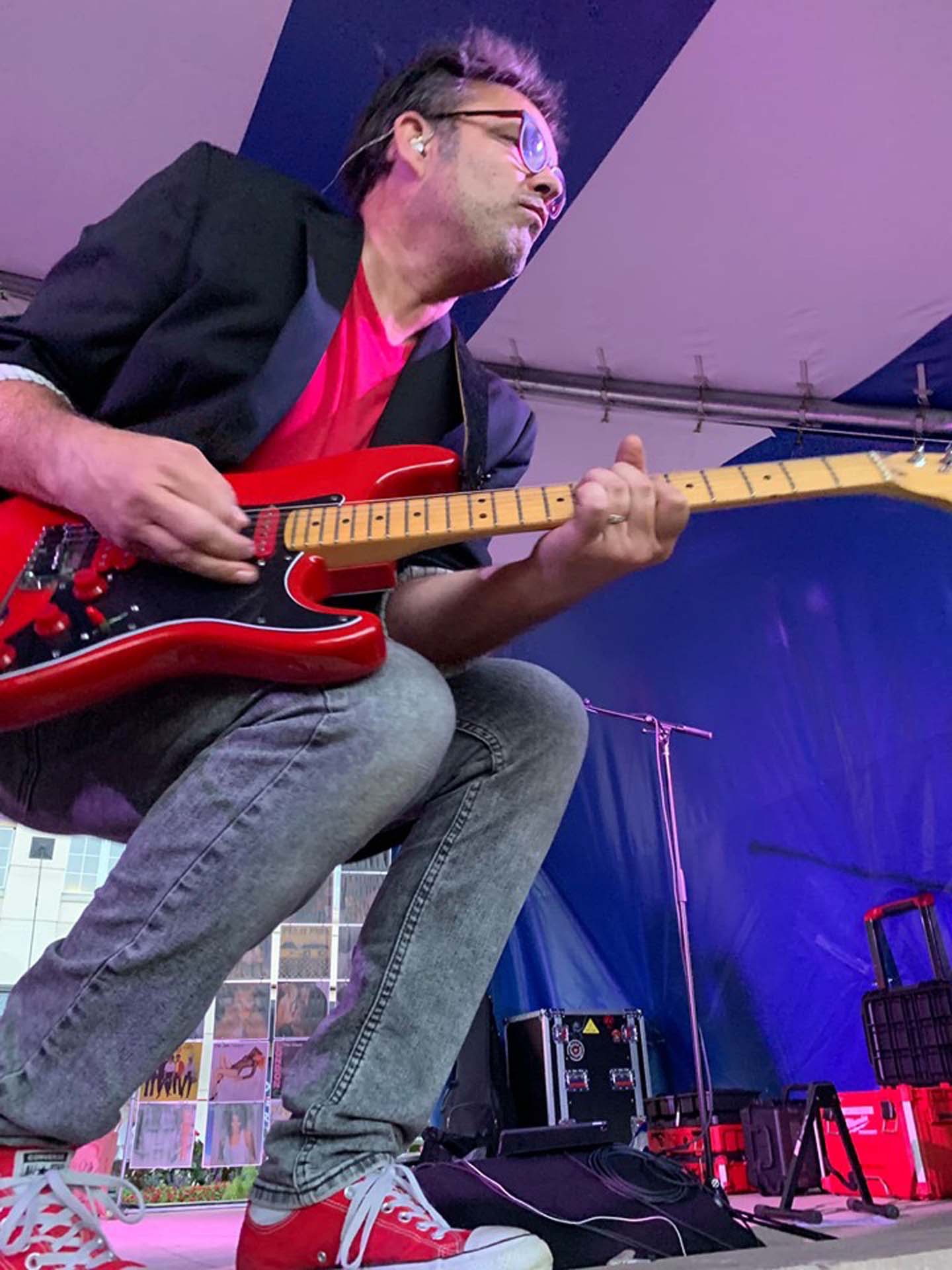 guy wearing red t-shirt and black suit jacket with jeans crouched down playing a guitar