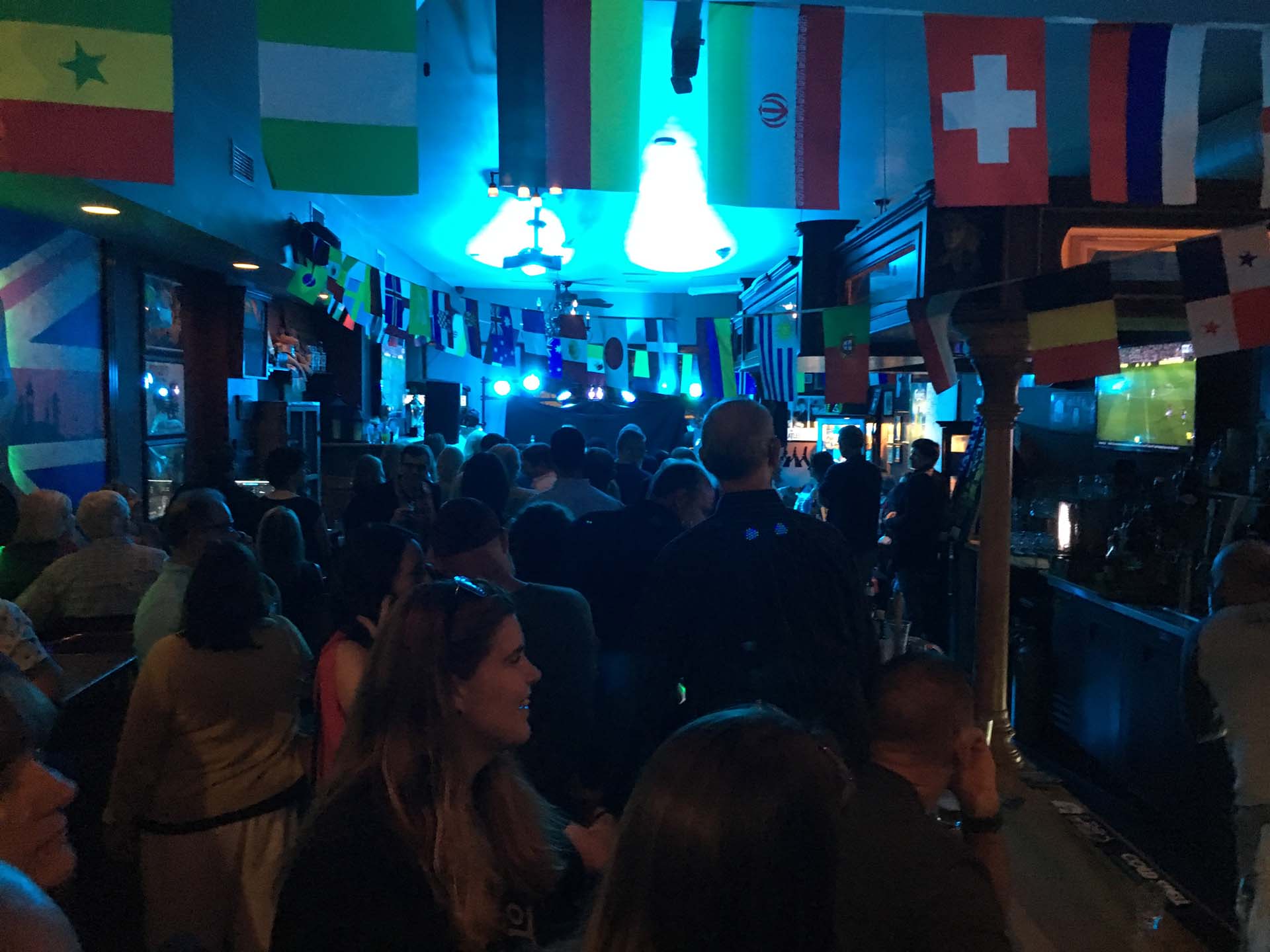image of crow watching band play on stage with different country flags hanging above streaming across the ceiling of the room